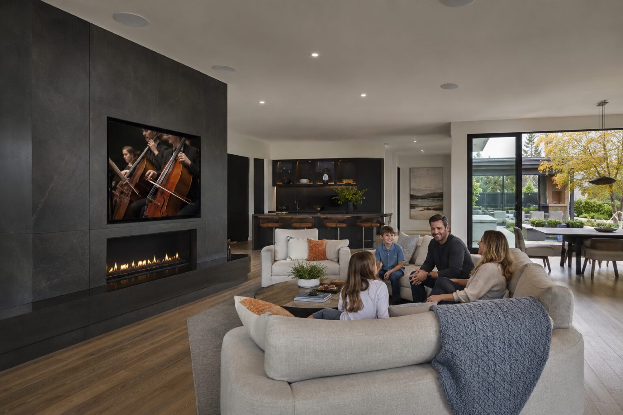 Family in a living room with in-ceiling speakers and a mounted television
